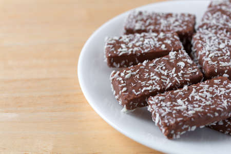 Side close view of several chocolate wafer cookies with coconut flakes on a white plate atop a wood...