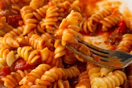 Close view of rotini pasta in a sausage and tomato sauce on a plate with a forkful of food.