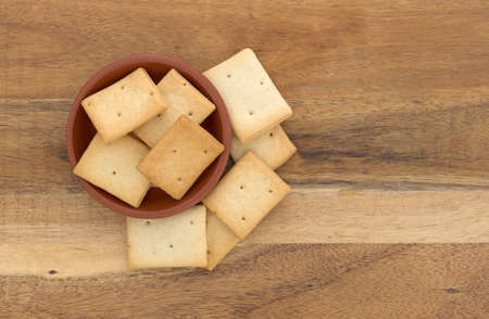 Top view of several hard bread crackers in a bowl and on a wood table.の写真素材