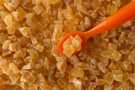 Top close view of sugar coated dried diced peaches with an orange plastic spoon illuminated with window light.の写真素材