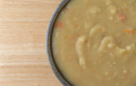 Top close view of a bowl of home style potato soup in a stoneware bowl atop a wood table top.