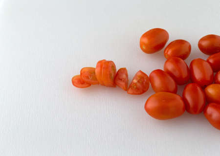 Several ripe grape tomatoes whole and sliced on a white plastic cutting board.の写真素材