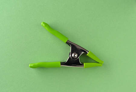 Top view of a metal spring clamp with plastic protectors on green paper.の写真素材