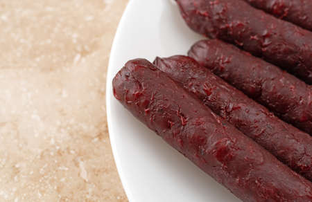 Close view of several barbecue flavor small smoked pork sausages on a white plate atop a brown...