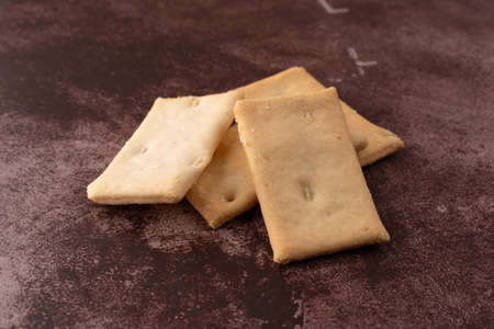 Side view of a serving of cheese flavor crostini crackers on a maroon counter top illuminated with...