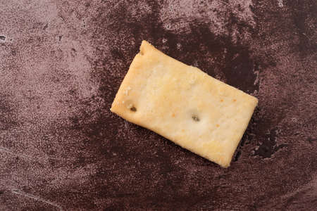 Overhead view of a single cheese flavor crostini cracker on a maroon counter top illuminated with natural lighting.の写真素材