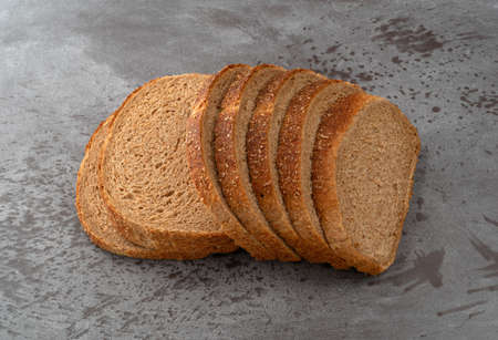 Several slices of all natural stone ground whole wheat bread on a gray counter top.