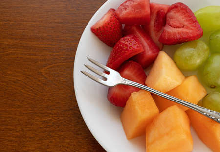 Overhead view of strawberries grapes and cut cantaloupe on a white plate with a small fruit fork...