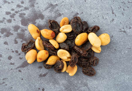 Top view of a small portion of peanuts and raisins on a gray background illuminated with natural...