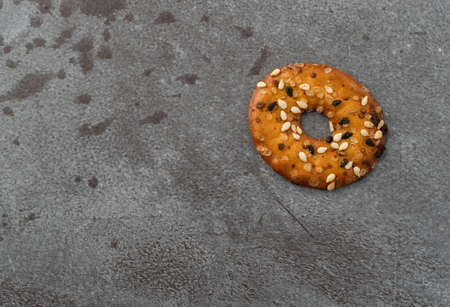 Top view of a single bite size bagel chip with assorted seeds on a gray background illuminated with natural light.の写真素材