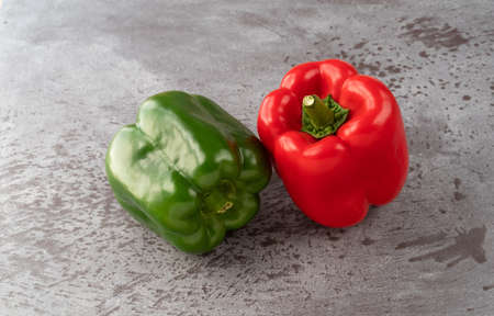 Side view of whole red and green bell peppers on a gray counter top.の写真素材