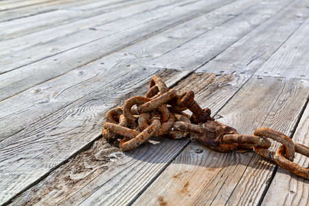 An old rusty chain sitting on a wood dock in the early morning light.の写真素材