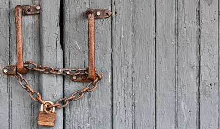 A very old padlock and chain attached to iron hand bars attached to a wood sliding door.の写真素材