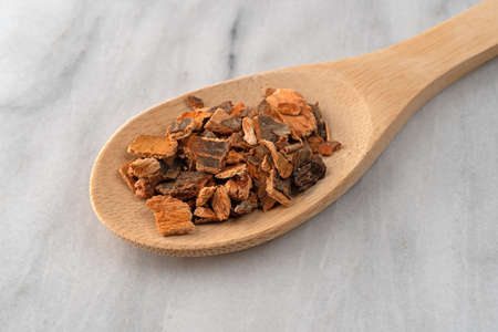 Small portion of wild cut cherry tree bark on a wood spoon atop a gray marble counter top.