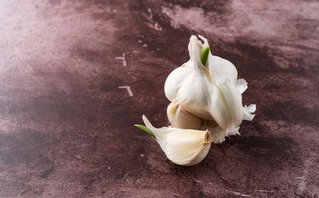 Side view of a sprouting garlic clove in front of a group of cloves on a red background.