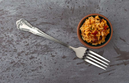 Overhead view of a small bowl of Mexican rice and beans with a fork to the side on a gray background...
