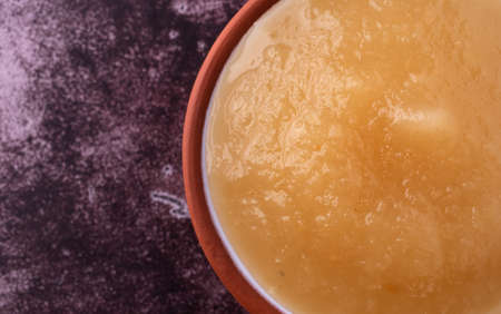 Overhead close view of a small bowl filled with sugar free applesauce on a maroon background.