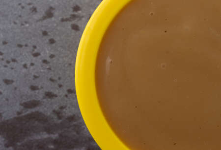 Overhead close view of brown turkey gravy in a small yellow bowl on a gray background.