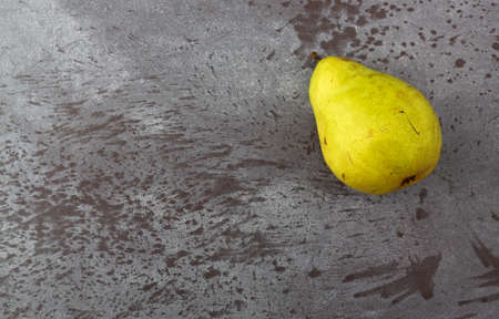 Top view of a single ripe green anjou pear offset on a gray mottled background illuminated with natural lighting.の写真素材