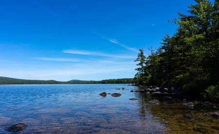 Wide view of the shoreline of Branch Lake with blue sky above and wispy clouds on a summer day in...