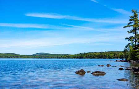 Wide view of rocks near the shore of Branch Lake with blue sky above and wispy clouds on a summer day in Maine.の写真素材