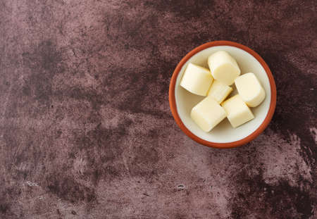 Top view of mozzarella string cheese pieces in a small bowl offset on a red background illuminated with natural lighting.の写真素材