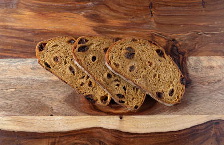 Top view of three pumpkin raisin bread slices on a wood cutting board illuminated with natural...