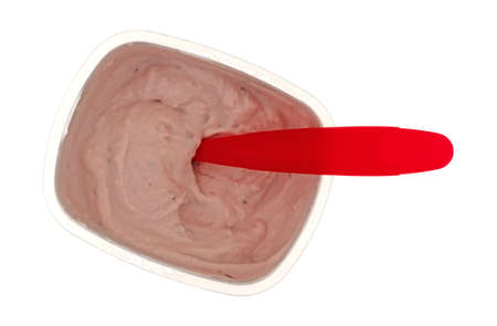 Overhead view of a small container of red raspberry yogurt with a spoon in the food isolated on a...