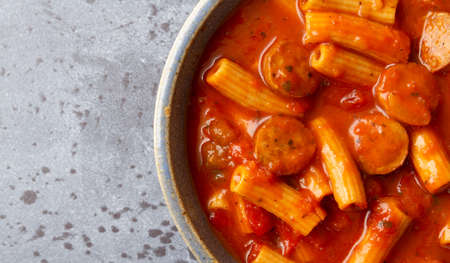 Top close view of rigatoni pasta and sausage in an old stoneware bowl on a gray background illuminated with natural lighting.の写真素材