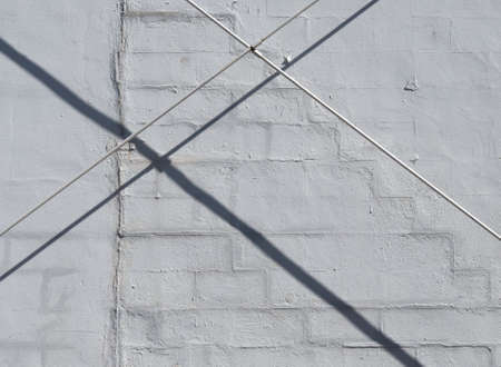 Two metal pipes crossing in front of an old painted concrete wall with shadows in the early morning...