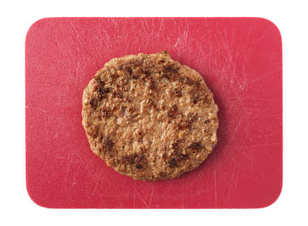 Single fried all beef lean hamburger patty on a red cutting board isolated on a white background.の写真素材
