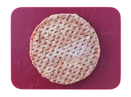 Top view of a frozen all beef lean hamburger patty atop a red cutting board isolated on a white background.の写真素材
