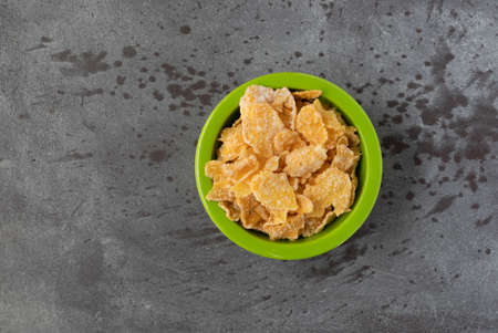 Top view of generic frosted corn flakes in a green bowl on a gray background.