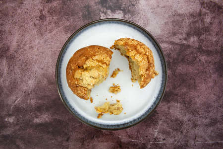 Single cinnamon crumb muffin broken in pieces on a plate atop a maroon tabletop top view.の写真素材