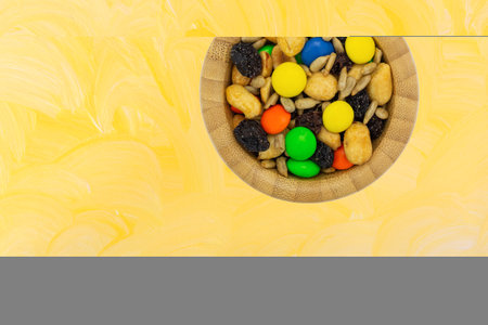 Sweet and salty trail mix in a bowl on a yellow painted background overhead view.の写真素材