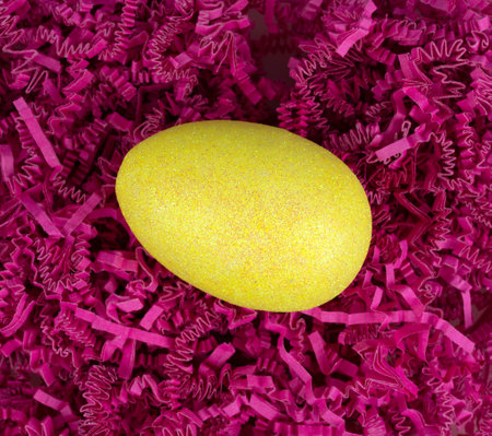 Top view of a yellow glitter easter egg atop dark pink shredded crinkle paper.