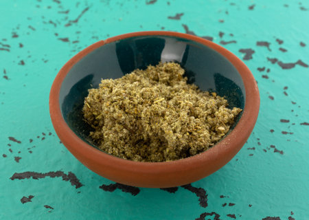 Side view of a small bowl of crushed sage leaf atop a green and black tabletop.