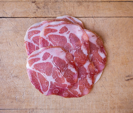 Overhead view of dry coppa on an old wood cutting board illuminated with natural light.