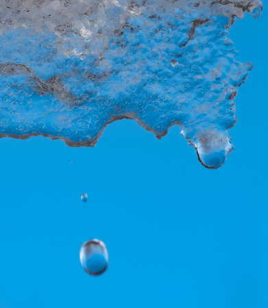 Abstract image of textured melting ice with water droplets falling against a deep blue background.の写真素材
