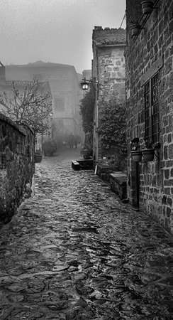 Black and white image of a couple walking down a narrow stone road on a foggy day in the town of Civita di Bagnoregio in Italy.の写真素材
