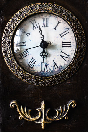 Close up image of an antique clock face and metal decoration below on a dark background. The time shows a few minutes before 6 and includes a seconds hand.の写真素材