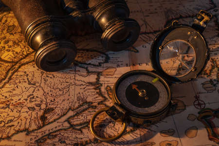 Image of an old compass with a cracked glass and binoculars sitting on map cast in warm candle light.の写真素材