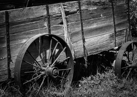 Black and white image of an old wooden cart with rusted metal wheels. The wood is weathered and rotting. The viewer gets a good impression of what life and transportation was likeの写真素材