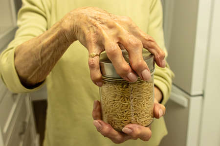 Close up image of an elderly woman with arthritis in her hands trying to open a jar of food. It...