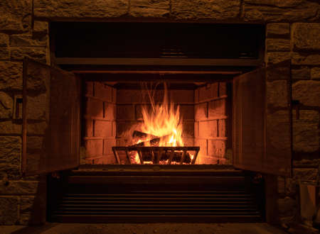 Image of a roaring fire in a stone enclosed fireplace. The flames show blurred motion and the embers are glowing red. The viewer is left with a sense of warmth and coziness.の写真素材