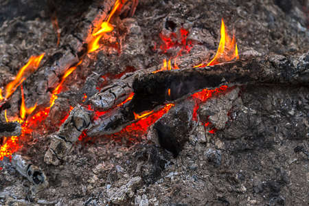 Embers and flames lick at wood glowing red & orange in the nightの写真素材