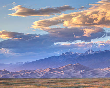 Sun sets on the Gread Sand Dunes backed by snow capped mountains.の写真素材