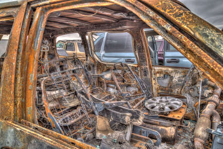 A hubcap is driving a burned out wreck of a car in a salvage lotの写真素材