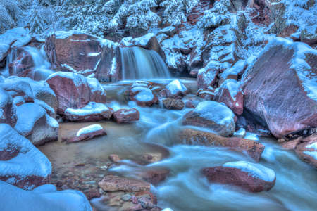 Early morning light finds fresh snow on boulders as water rushes by.の写真素材