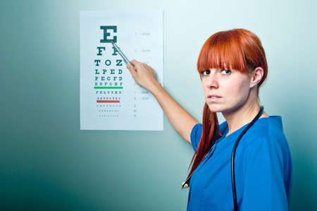 female oculist doctor examining patient with an eye chart behindの写真素材